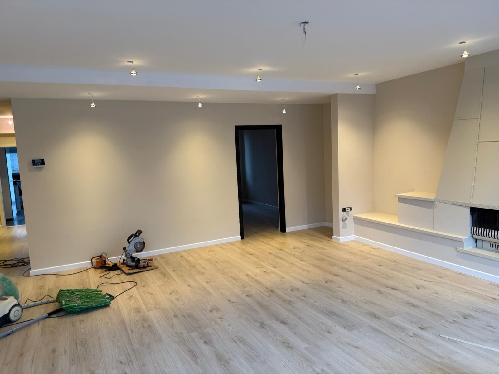 Dezelfde woonkamer na de klus: lichte wanden, spots in het plafond en een lichte vloer