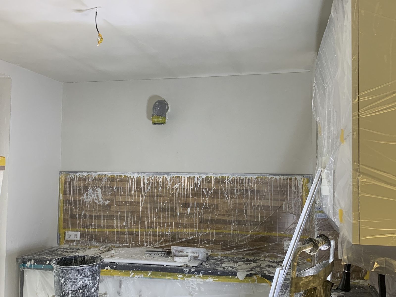 Keukenwand en plafond net gestuct, met de achterwand en kastjes afgeplakt onder plastic en geel afplakband